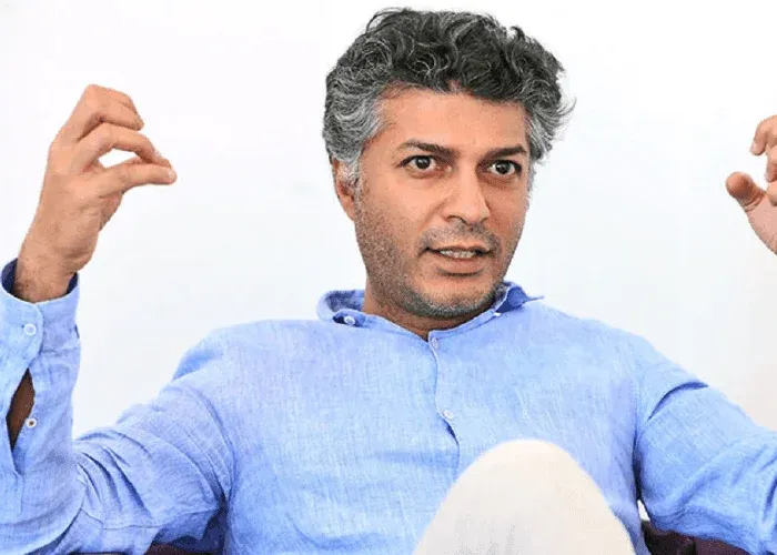 Person gesturing while speaking, wearing blue shirt.