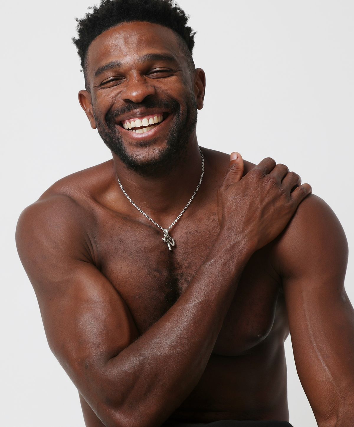 Smiling man with necklace, showing bare shoulders.