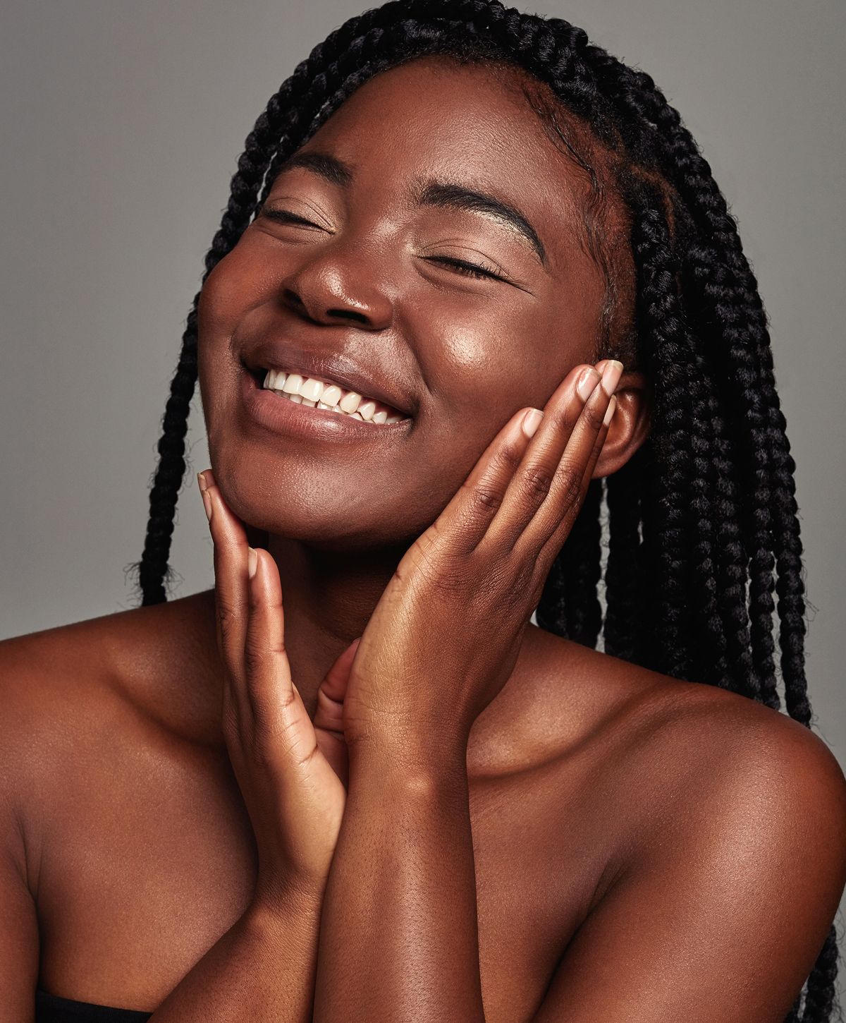 Smiling person with braided hair and glowing skin.