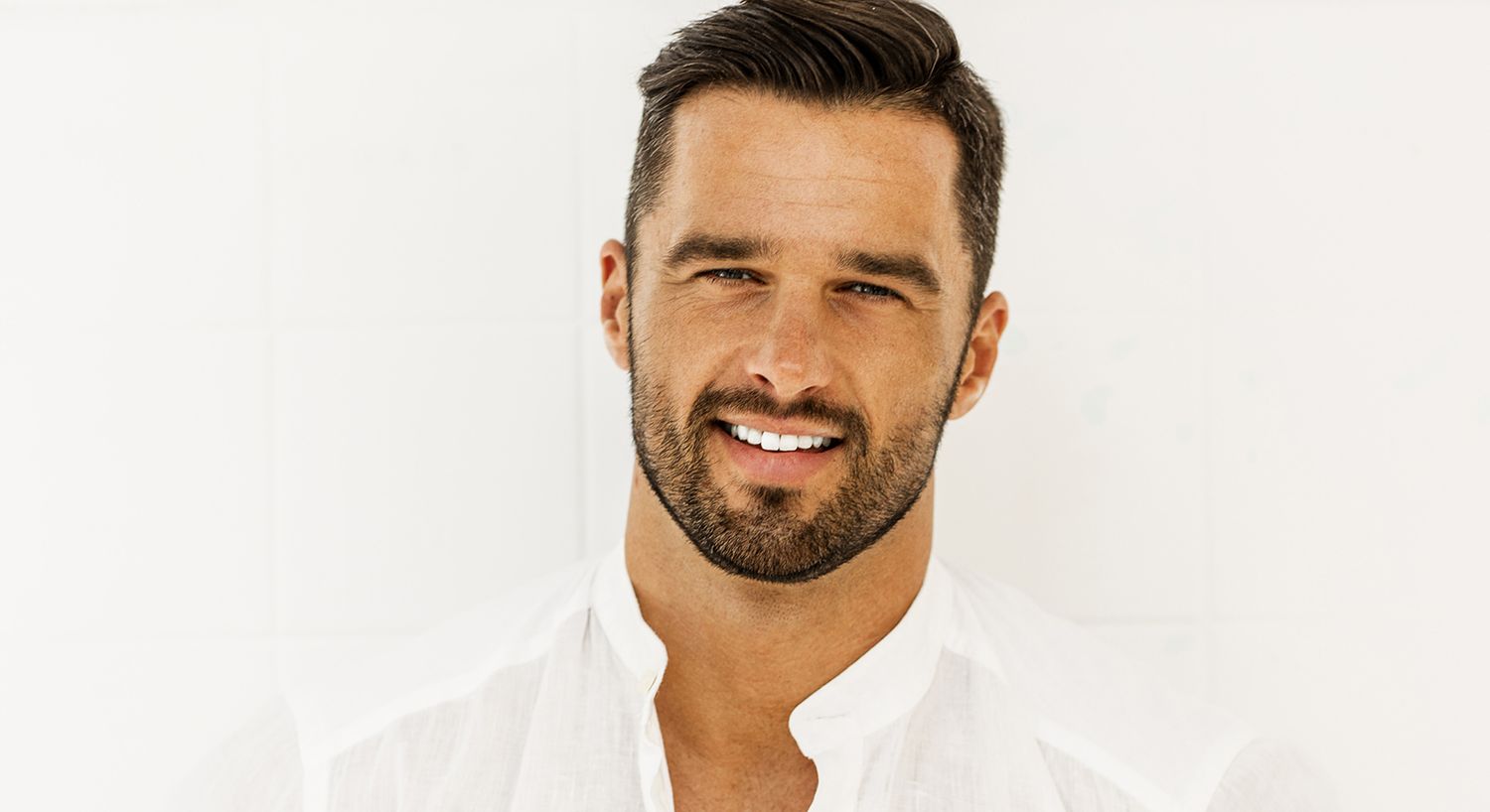 Smiling man in a white shirt against light background.