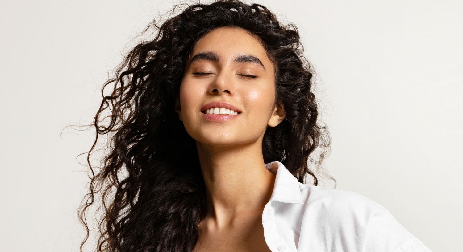 Smiling woman with curly hair and closed eyes.
