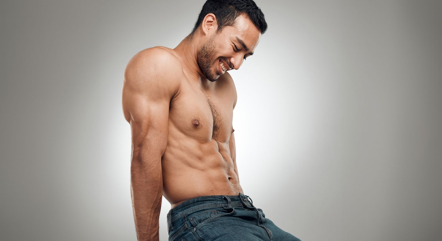 Muscular man sitting and smiling playfully.