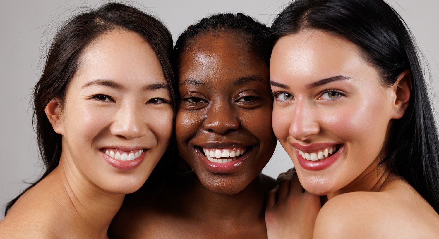Three women smiling together, diverse backgrounds.