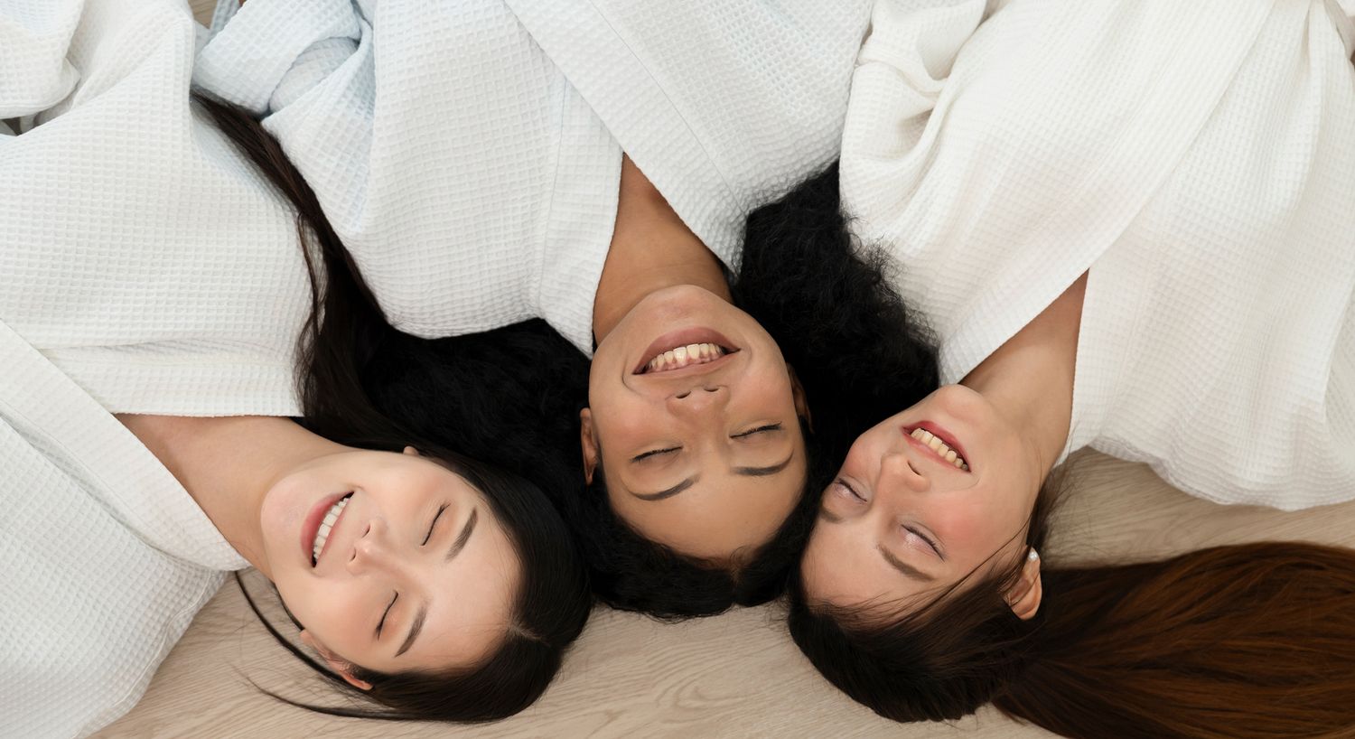 Three women smiling together in white robes.