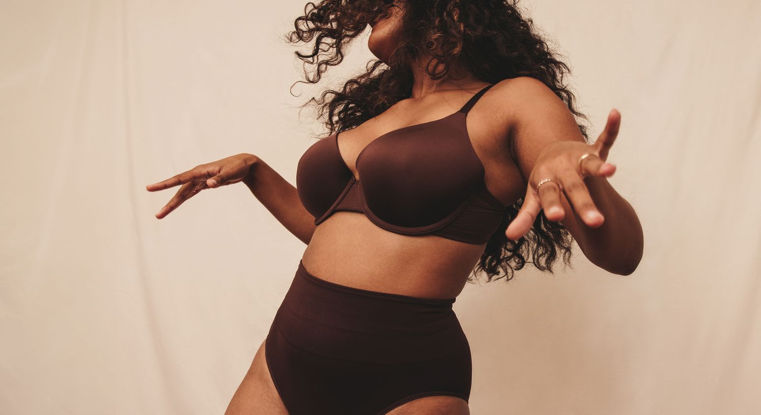 Woman dancing in brown lingerie against neutral background.